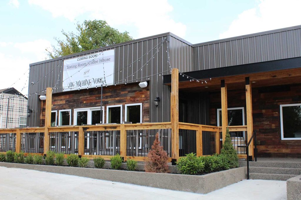 Modern metal building with rustic wood siding, covered porch, deck seating, and landscaping—ideal for a café, tasting room, or retail space.
