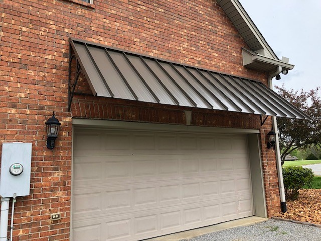 Brick home garage with brown standing seam metal awning roof panels above double garage door, adding durable, modern curb appeal.