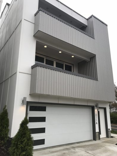 Modern townhouse with exposed fastener metal siding panels, gray vertical steel cladding, balcony, and white garage door facade.