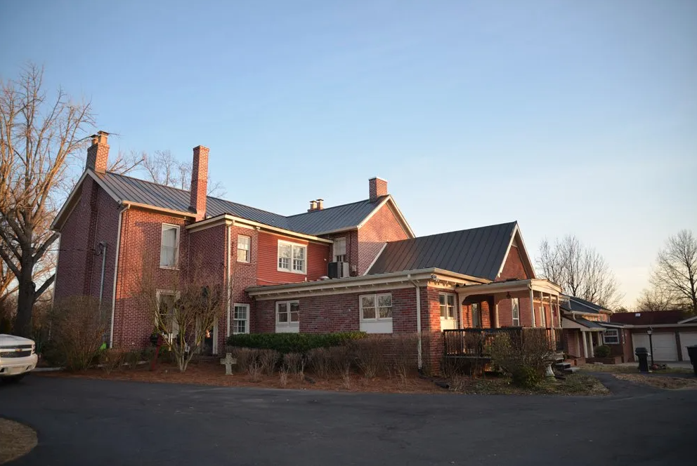 Brick home with gray standing seam metal roofing panels, multiple gables, chimneys, and covered porch at sunset.
