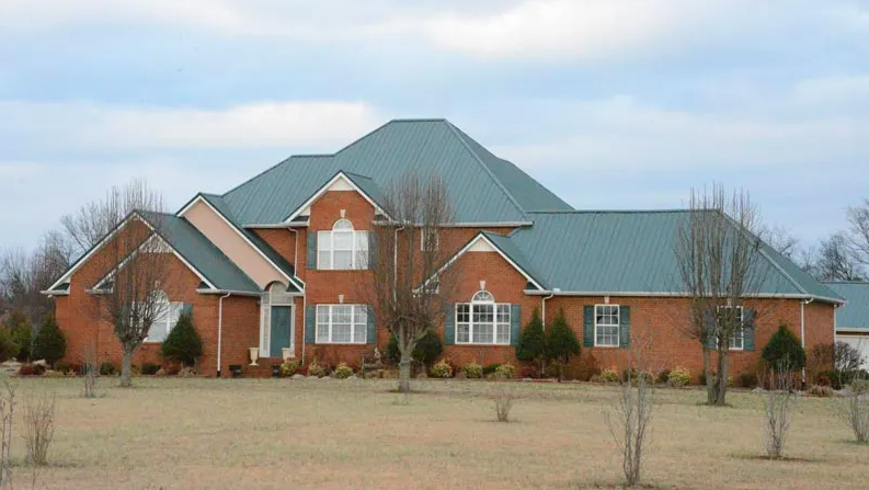 Brick home with green standing seam metal roofing panels, multiple gables, and large windows on a spacious landscaped lot.